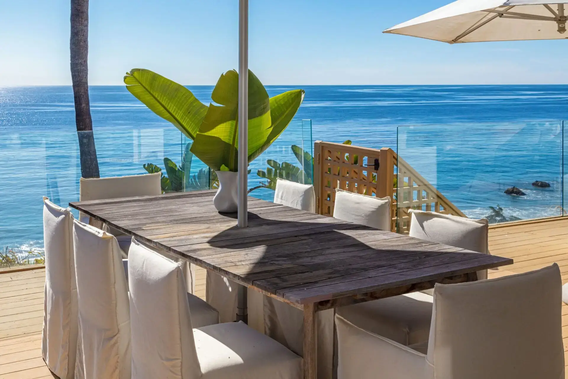 The outdoor dining table on Carrara's Malibu deck, wooden stairs down to the beach and the ocean beyond