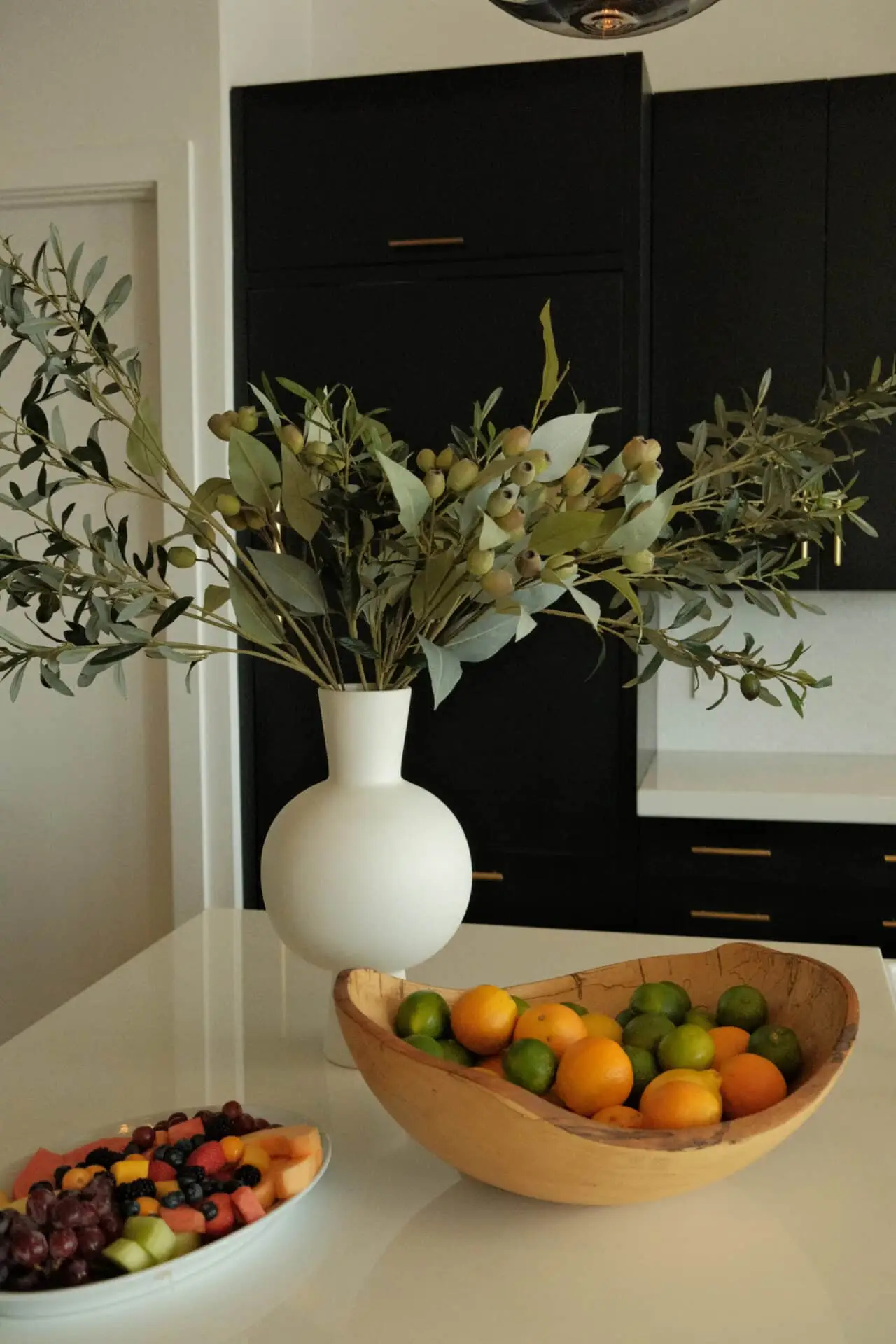 Fruit on the kitchen counter at the Carrara house, a wooden bowl of limes and oranges beside cut melon, grapes and blueberries