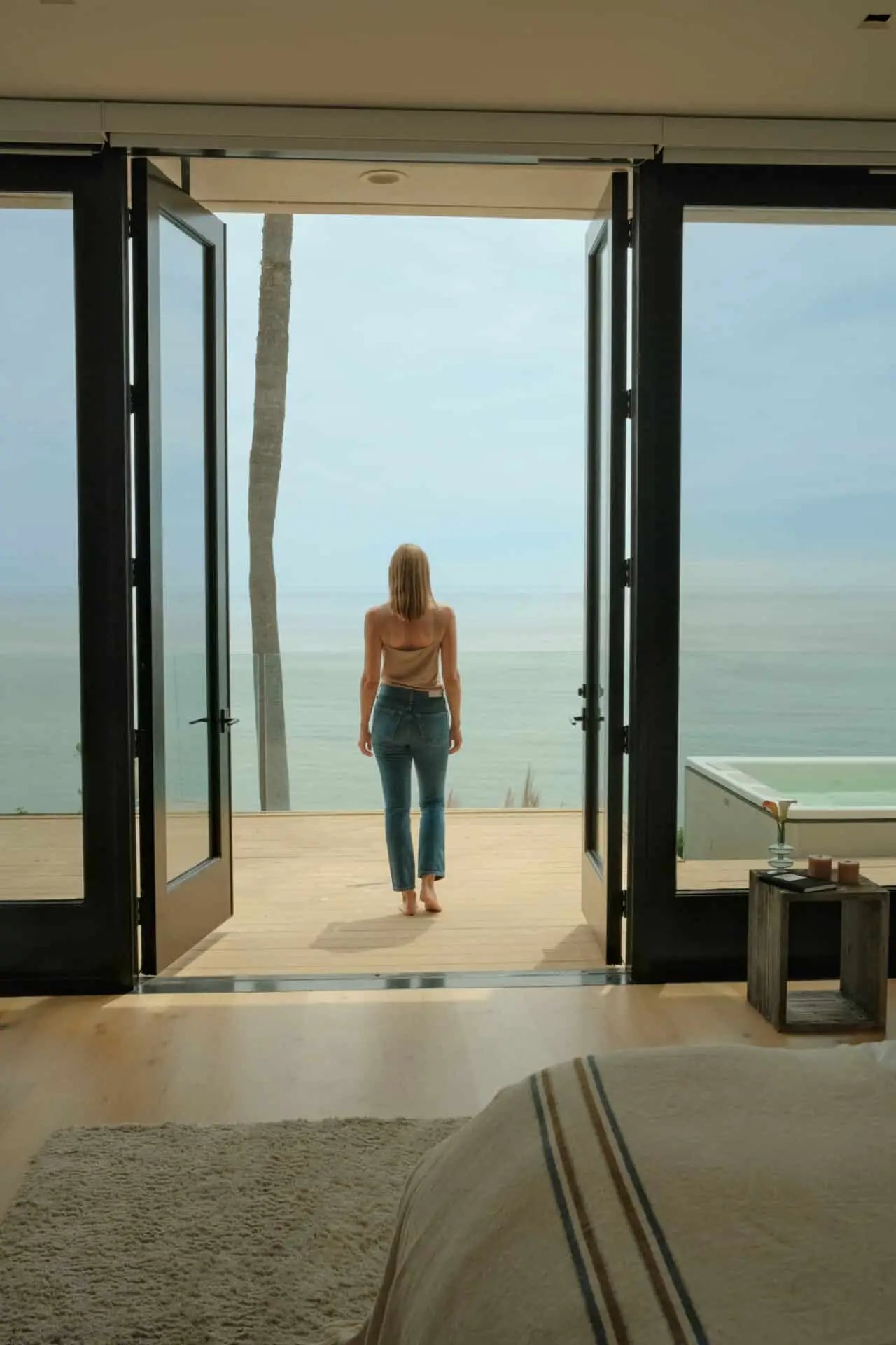 A woman walking barefoot from a suite at Carrara in Malibu onto the deck toward the ocean, seen from behind