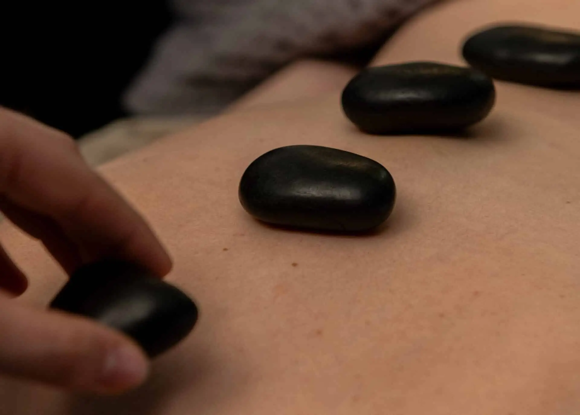 Black stones laid along a client's back during a massage, the therapist's hand setting one more in place
