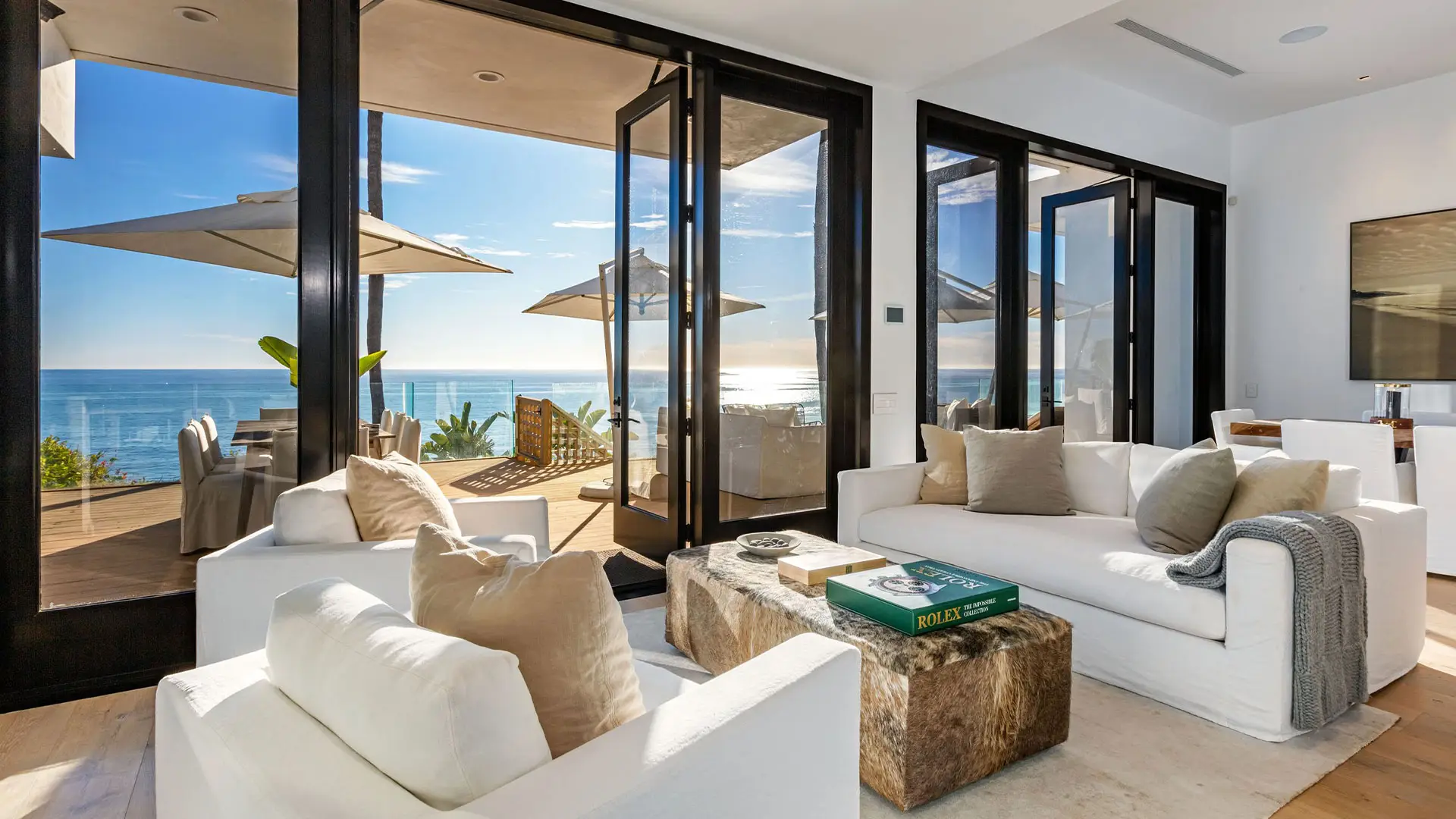 The great room of the Carrara beach house, white sofas and folding glass doors open to the deck and the ocean