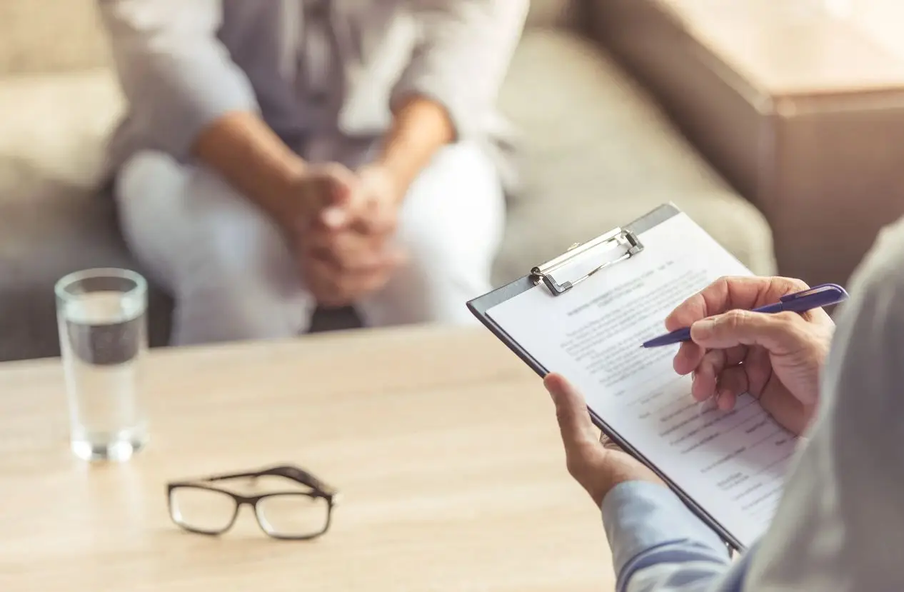 A clinician writing on an intake form across a table from a client, both faces out of frame