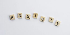 Scrabble tiles spelling "ANXIETY" arranged in a curved line on a plain white background.