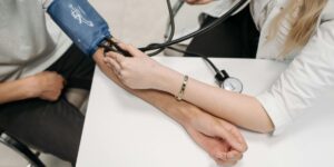 Healthcare professional measuring patient's blood pressure with arm cuff and stethoscope on white table.