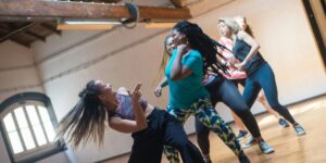 Diverse group of women dancing energetically in a studio with wooden floors and beamed ceiling.
