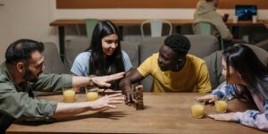 Diverse group playing Jenga at table with orange juice, in casual indoor setting.