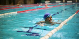 Smiling swimmer in blue cap and goggles rests in pool lane during training session.