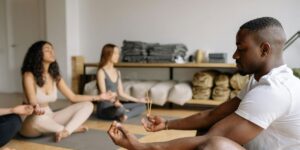 Three people meditating on yoga mats in a studio, sitting cross-legged with eyes closed