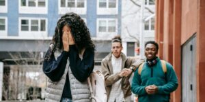 Young woman covers face while two smiling men stand behind her outdoors near buildings.