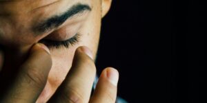 Close-up of person rubbing eyes, showing fatigue or discomfort against dark background.