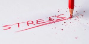 Red pencil writing "STRESS" on white paper, surrounded by pencil shavings and debris.