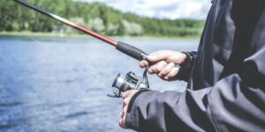 Angler holding fishing rod and reel over lake, surrounded by trees on shoreline.