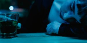 Dimly lit bar scene: person slumped on table next to glass of green liquor.