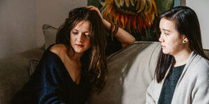 Distressed young woman on couch during family intervention, with concerned family member beside her.