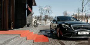 Luxury black Mercedes-Benz parked in front of building entrance with red carpet on steps, winter scene in background