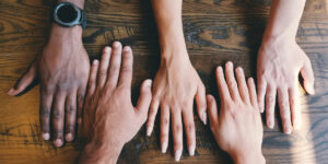 Diverse hands of family members placed together on wooden table, symbolizing support and unity.