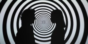 Silhouettes of two people against a black and white spiral background, suggesting an psychedelic experience