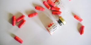 Small medication vial surrounded by scattered bright red capsules on a white surface