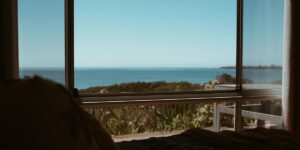 A view from a window overlooking a lush, green landscape and the ocean in the distance.