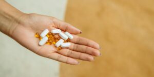 A person's hands holding a variety of white and yellow pills or capsules.