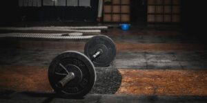 Black barbell on worn wooden gym floor with battle ropes in background