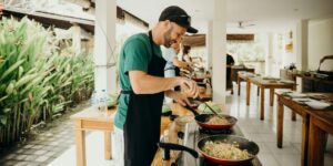 Chef in green shirt and black apron cooking with woks at outdoor cooking class