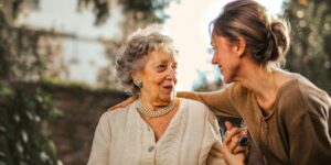 Young woman in brown sweater sharing warm moment with elderly woman wearing pearl necklace and cable-knit cardigan