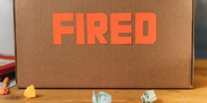 Cardboard box with orange text reading 'FIRED' with crumpled papers scattered in front