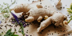 Fresh ginger root with purple flowers and spices scattered on wooden cutting board