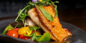 Seared fish fillet with colorful cherry tomatoes and arugula on dark plate