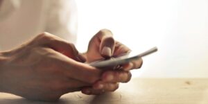 Close-up of hands using a smartphone on wooden surface in warm lighting