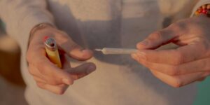 Close-up of hands holding a lighter and rolling paper with smoke visible