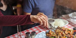 Hands cutting hot food at table with red checkered tablecloth