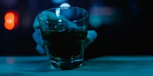 A shot glass containing green liquid photographed in blue ambient lighting