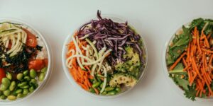 Three healthy poke bowls with colorful vegetables, edamame, and shredded cabbage