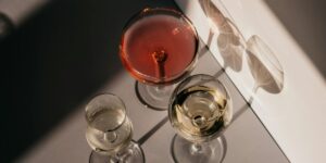 Three wine glasses containing rosé and white wines casting shadows in afternoon light