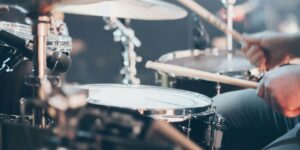 Close-up of a professional drum kit on stage showing cymbals, snare drum, and microphone setup, with soft lighting creating highlights on the metallic surfaces