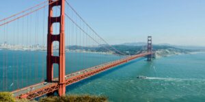 A panoramic view of the iconic Golden Gate Bridge in San Francisco stretching across the blue waters, with a boat sailing beneath and the city skyline in the background.
