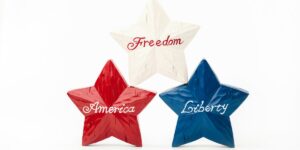 Three decorative stars painted red, white, and blue with the words 'America,' 'Freedom,' and 'Liberty' written on them, symbolizing core American values.
