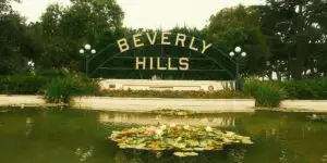The iconic Beverly Hills archway sign with gold letters over a lily pond with blooming water lilies and lush green trees