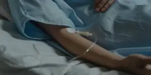 Close-up of a person in a hospital gown resting in bed with an IV line in their arm, illustrating the safety and medical monitoring provided during detox in a rehab setting.
