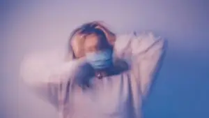 Blurred image of a person in distress clutching their head against a blue background