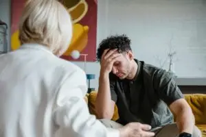 Man in therapy session holding his forehead while speaking with a counselor.