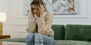 Woman sitting on a couch with her head in her hands next to a glass of water