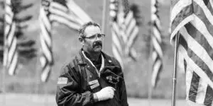 solemn black and white photograph of a military veteran standing respectfully among American flags, symbolizing the unique challenges of trauma, the invisible wounds of service, and the importance of specialized addiction recovery support for those who have served.