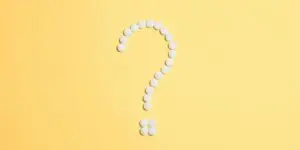 uestion mark formed from white medication pills on a yellow background.