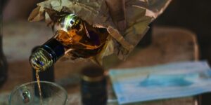 A close-up of a hand pouring amber liquor from a glass bottle wrapped in a brown paper bag, highlighting the reality of alcohol addiction, covert drinking behaviors, and the critical need for professional alcohol detox.