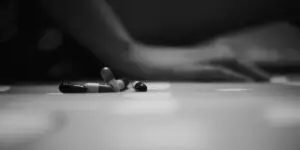 A stark black and white close-up of loose capsule pills scattered on a surface with a blurred, motionless figure in the background, illustrating the severe, life-threatening risks of accidental fentanyl poisoning and laced counterfeit medications.